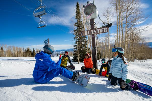 Clients and an instructor discuss snowboarding technique on a ski run underneath an art installation at Park City Mountain