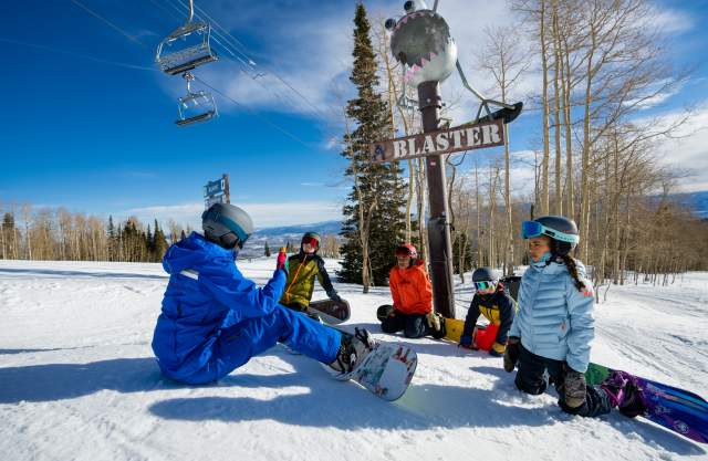 Clients and an instructor discuss snowboarding technique on a ski run underneath an art installation at Park City Mountain