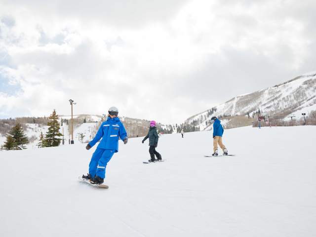 Two clients take a snowboard lesson with an instructor on a ski run at Park City Mountain