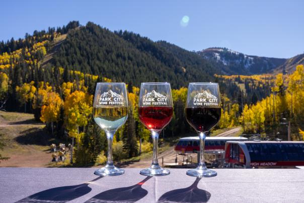 Three glasses of wine sit on a table in front of a mountain vista and colorful fall leaves in Park City, UT