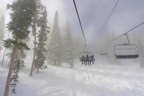 Three people riding up a chairlift through a cloudy morning