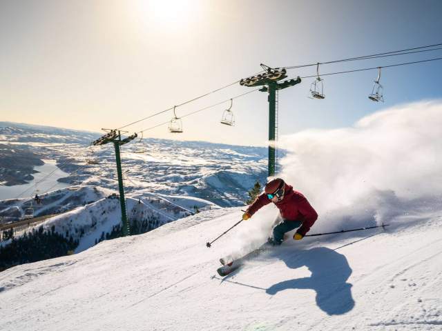 A skier carves a turn in front of a rising sun and chair lift at Deer Valley in Park City, UT