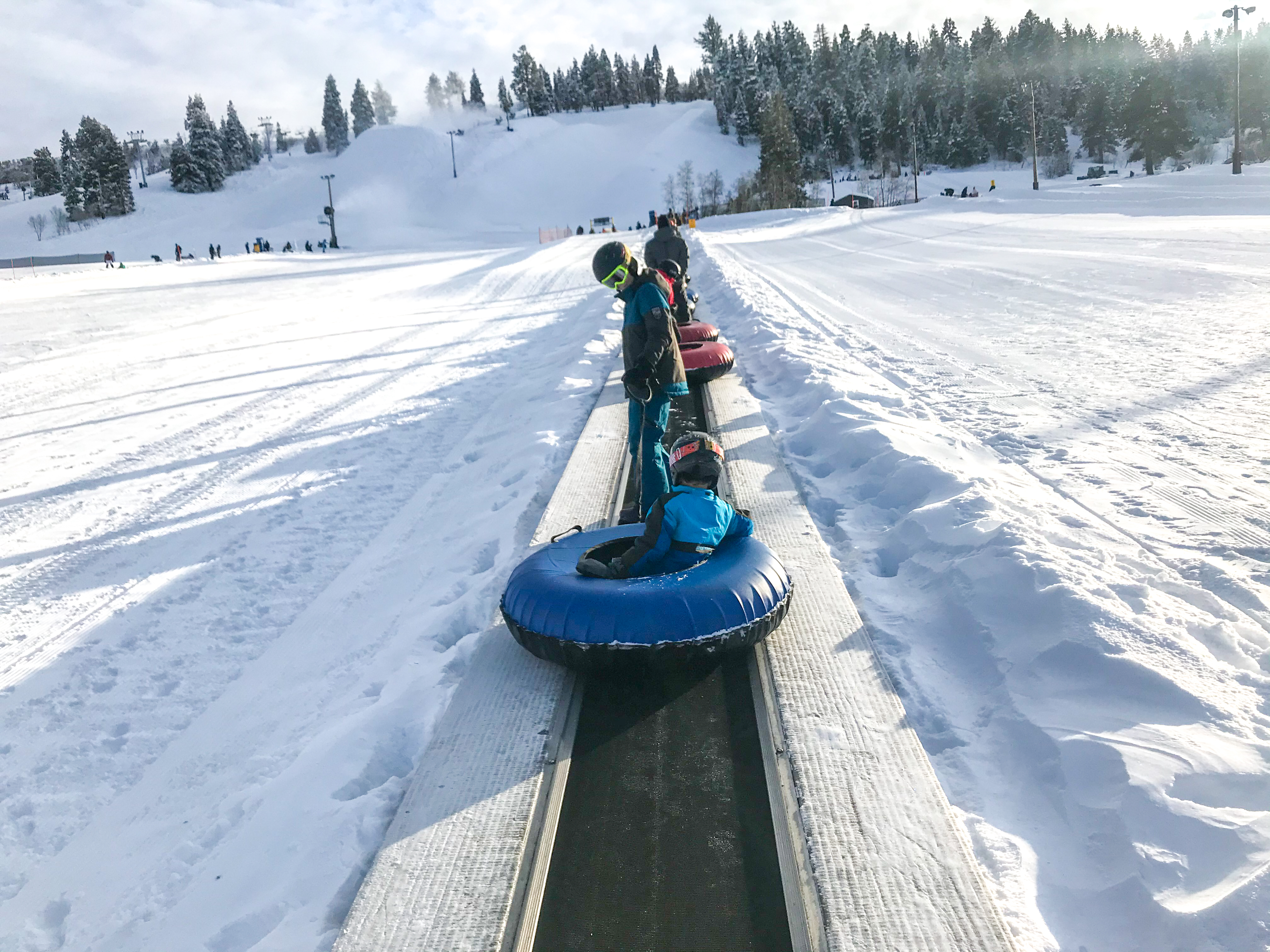 Boys riding up the hill on the magic carpet with tubes