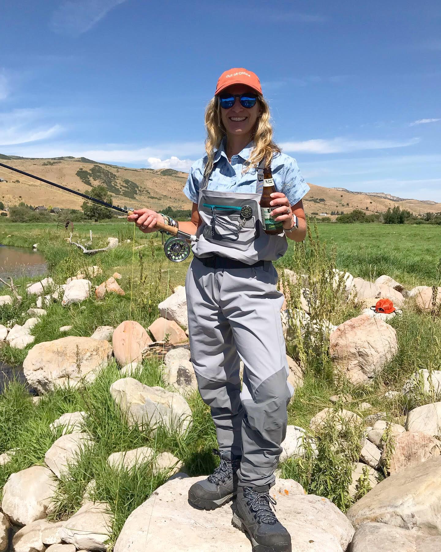 Person in waders holding a fishing pole and a beer