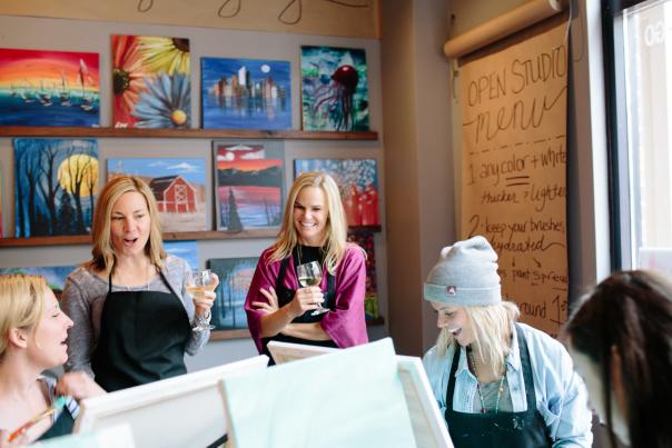 a group of women drinking wine and painting together