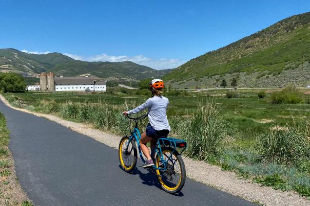 Woman riding an electric bike along a paved path with a white barn in the background