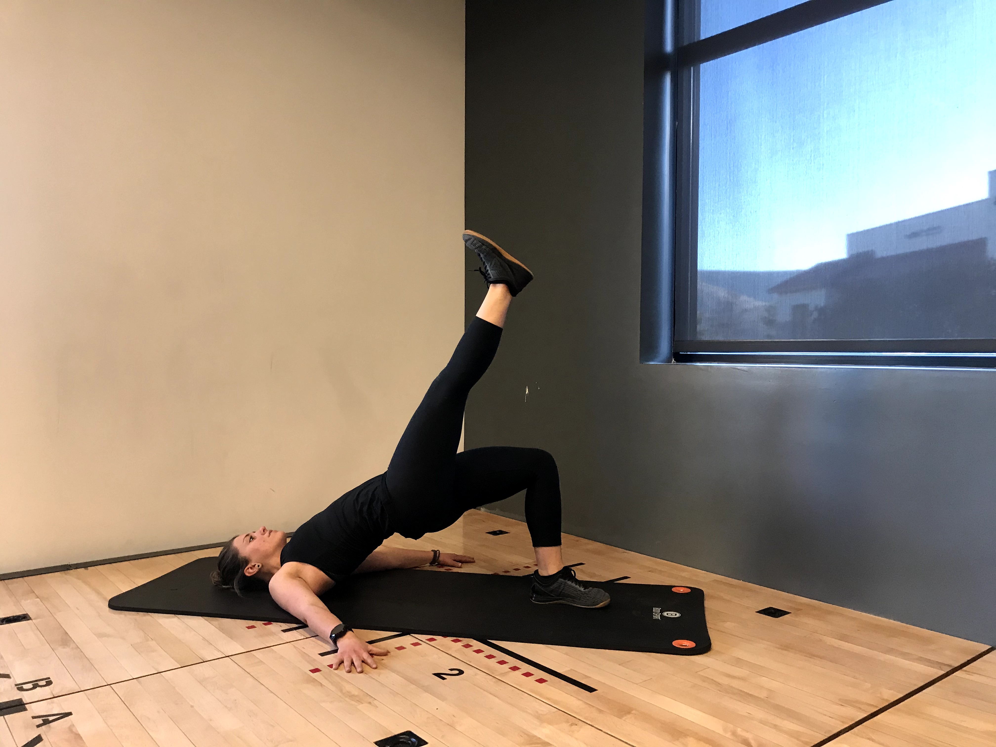 Instructor on floor demonstrating single leg glute bridge