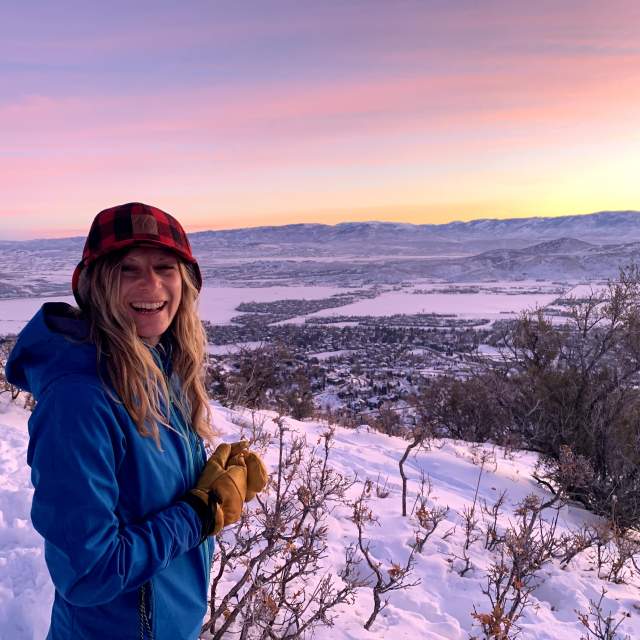 a woman poses for a photo with a colorful sunrise in the background