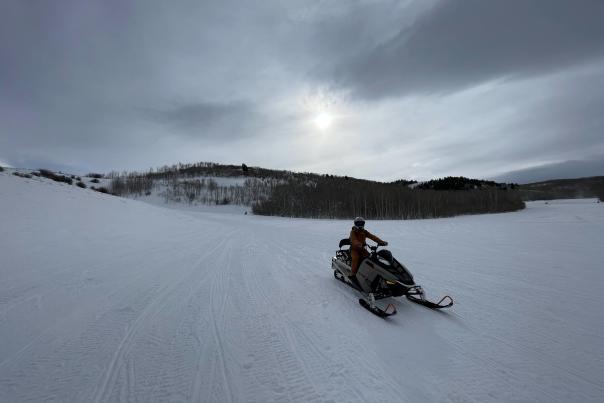 Person riding a snowmobile in a vast landscape of snow.