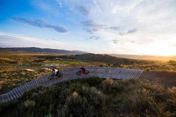 Two mountain bikers riding a rainbow rail in bike park