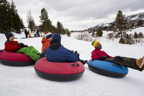 four teenagers tubing down a hill