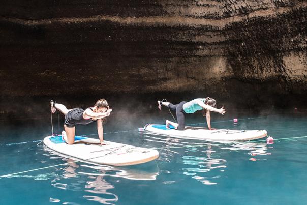 Two women on paddleboards doing yoga in a natural crater