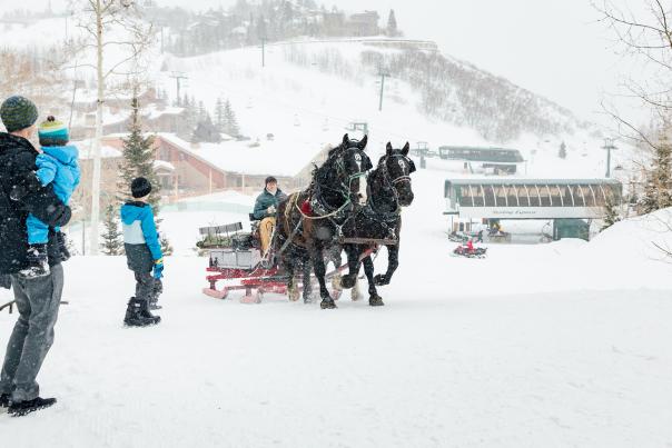 Father and sons waiting outside for sleigh ride on a ski run with snow falling at Deer Valley in Park City, UT